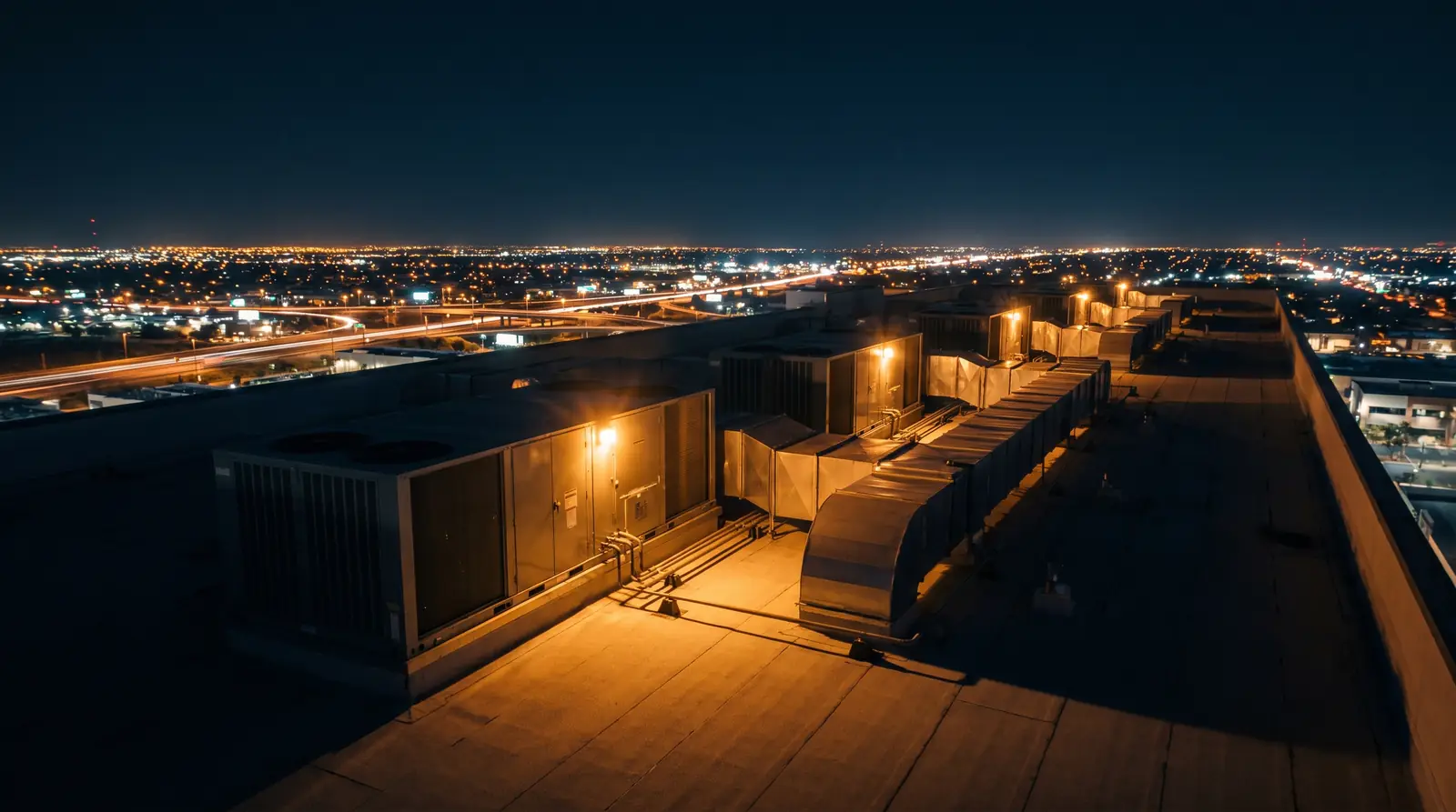 A row of commercial rooftop HVAC units at night above the Phoenix street grid