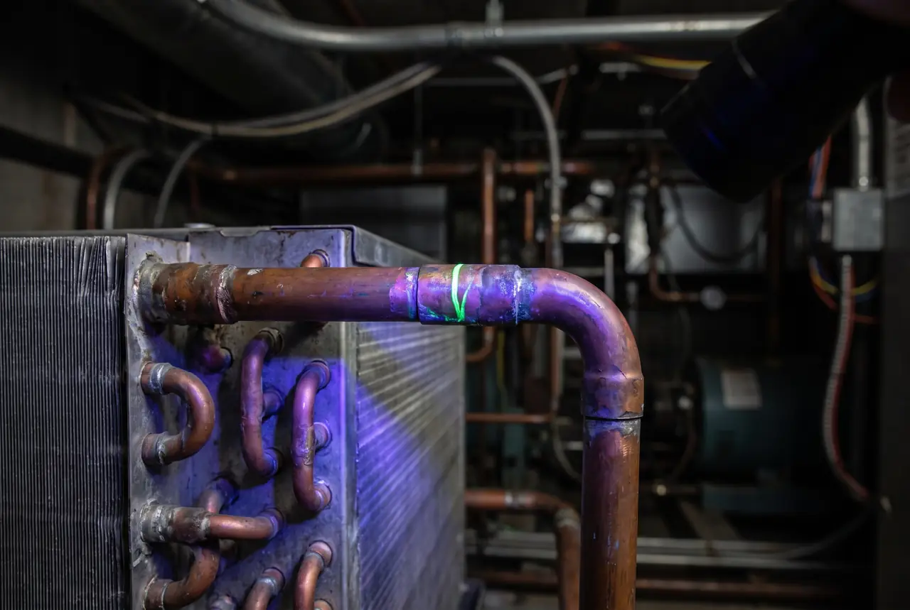 Brazed copper refrigerant lines under ultraviolet light showing fluorescent dye at a joint